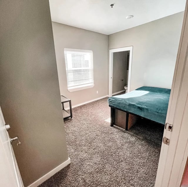 Bed with teal blanket small table and door bedroom at Fireside District Apartments in Stephenville Student Accommodation