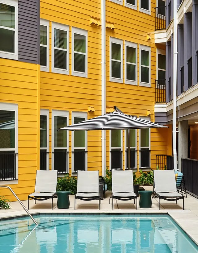 Chairs umbrella and pool by yellow building exterior at Flatiron in Baton Rouge Student Accommodation