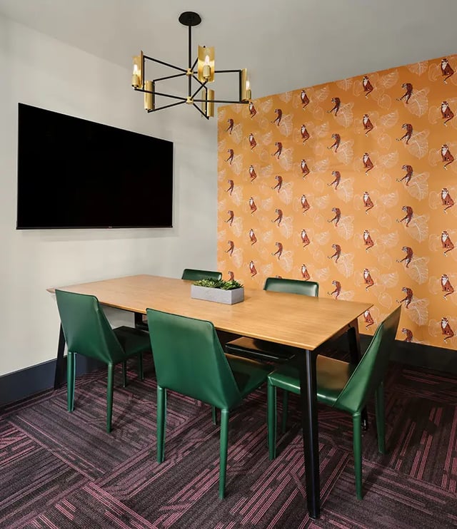 Wooden table green chairs large TV patterned wallpaper dining area at Flatiron in Baton Rouge Student Accommodation