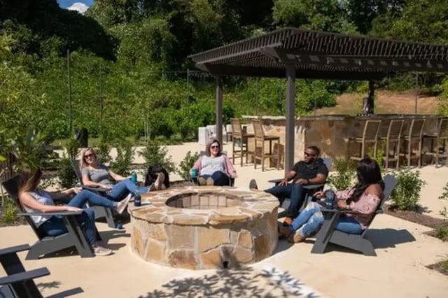 People relaxing by stone fire pit and bar area exterior at Flatts at South Campus in Oxford Student Accommodation