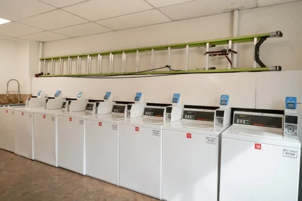 Row of white washing machines with blue displays laundry room at Monticello Apartments in Provo Student Accommodation