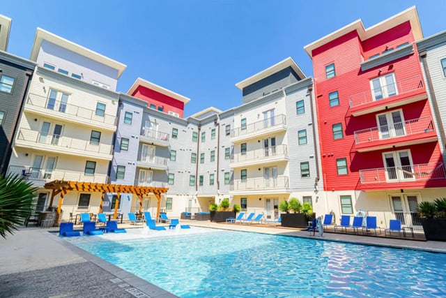 Pool with lounge chairs and colorful buildings exterior at Pointe San Marcos in San Marcos Student Accommodation