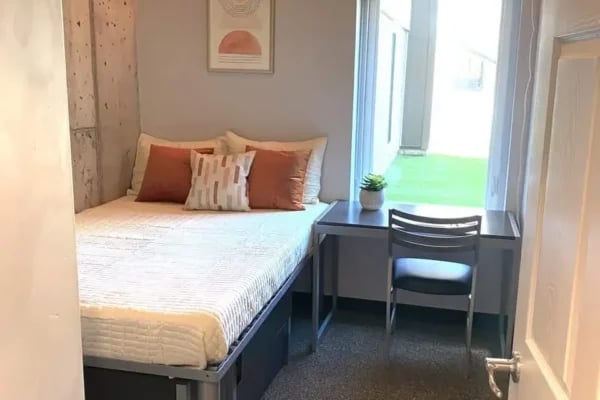 Bed with orange pillows desk chair plant bedroom at The Factory Student Housing in Logan Student Accommodation
