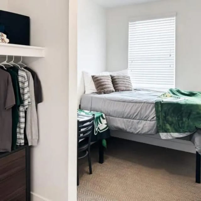 Clothes hanging on rack bed with green throw bedroom at Promenade Place in Orem Student Accommodation