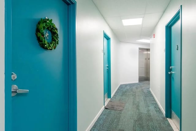 Turquoise doors wreath carpeted hallway interior at The Gates in East Lansing Student Accommodation