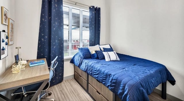 Blue bed desk chair artwork and blue curtains bedroom at Haven At Elgin in Houston Student Accommodation