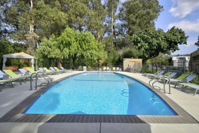 Pool with lounge chairs and trees exterior at Mustang Village Apartments in San Luis Obispo Student Accommodation