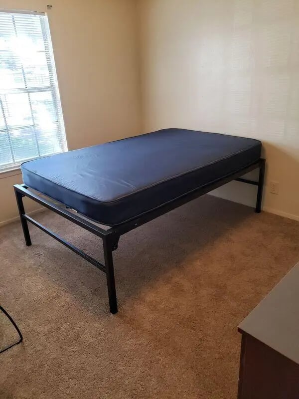 Black metal bed frame with blue mattress bedroom at Baylor Plaza III in Waco Student Accommodation