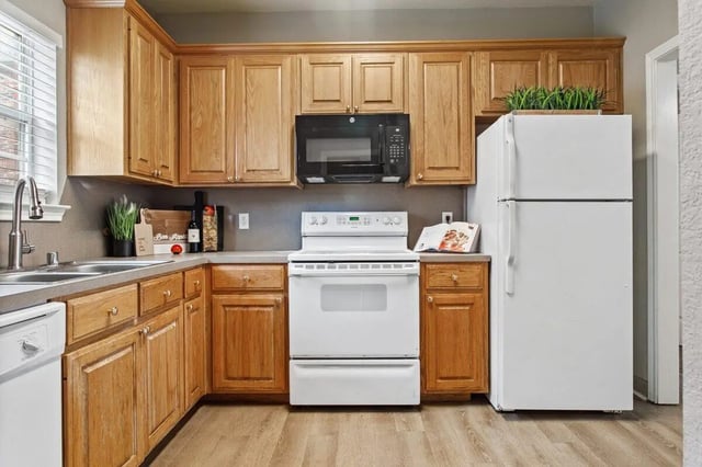 Wooden cabinets white stove microwave refrigerator kitchen at Bear Crossing Apartments in Waco Student Accommodation