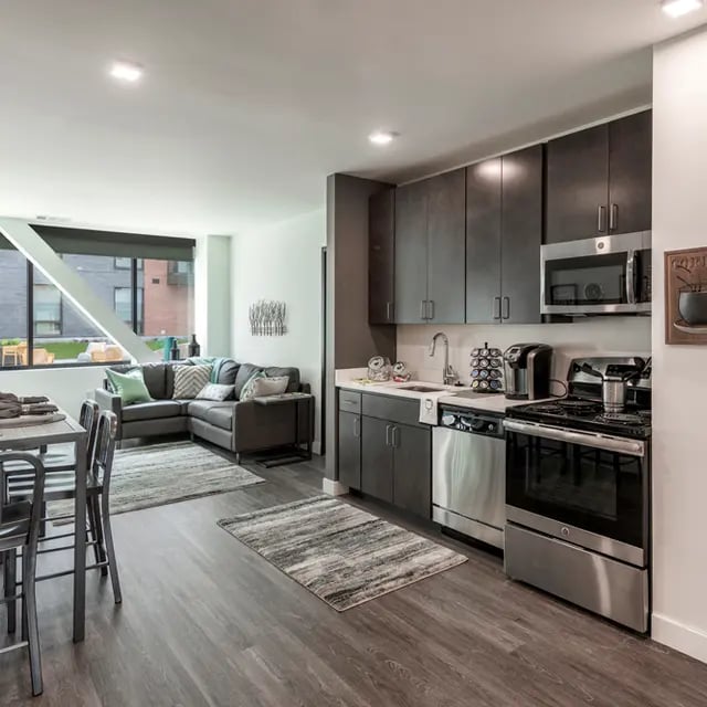 Lounge and kitchen with sectional sofa stainless appliances living room kitchen at 505 on Walnut Apartments in Syracuse Student Accommodation