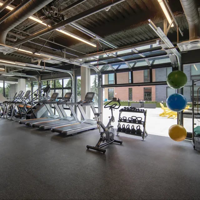 Treadmills stationary bike weights and large garage door opening to outdoors playing area at 505 on Walnut Apartments in Syracuse Student Accommodation