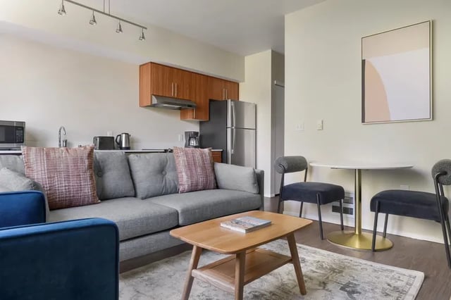 Grey sofa patterned pillows coffee table dining set living room at Clara Apartments in Seattle Student Accommodation