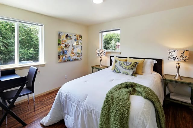 Bed desk chair artwork lamps and green throw bedroom at Clara Apartments in Seattle Student Accommodation