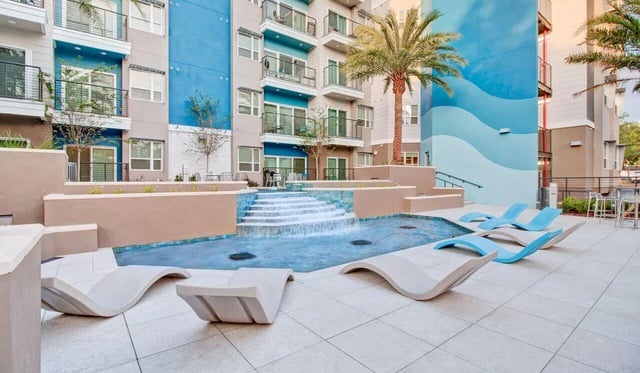 Pool with waterfall lounge chairs and palm trees exterior at Cascades Luxury Apartments in Gainesville Student Accommodation