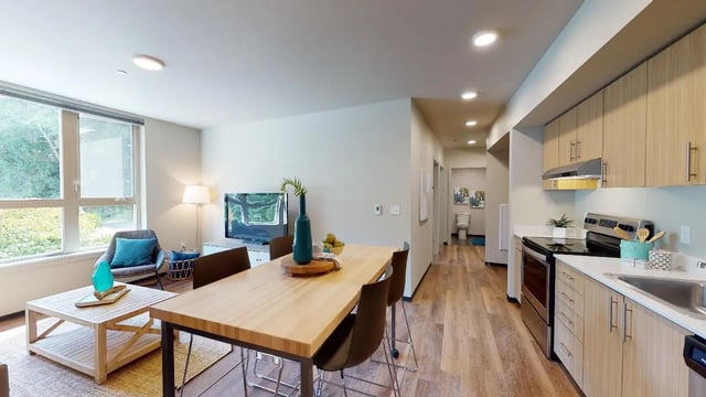 Wooden table chairs television and kitchen living area at 7000 Campus Living Apartments in Shoreline Student Accommodation