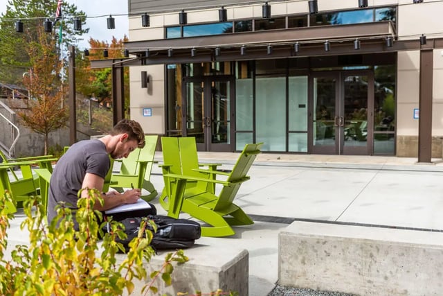 Student studying outside with green chairs exterior at 7000 Campus Living Apartments in Shoreline Student Accommodation