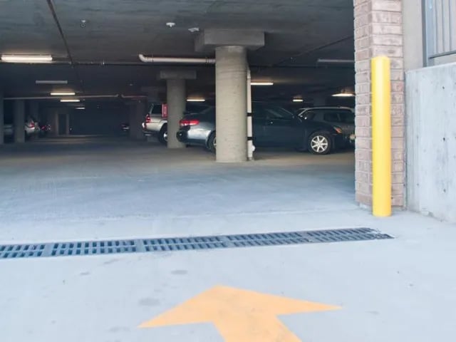 Cars in covered parking garage with yellow bollard Exterior at The Towers Two - Women Approved Housing in Rexburg Student Accommodation