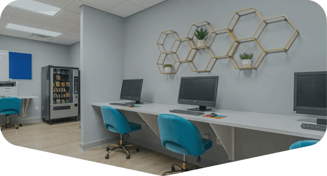 Computer stations with blue chairs and vending machine study area at Hawks Landing in Oxford Student Accommodation