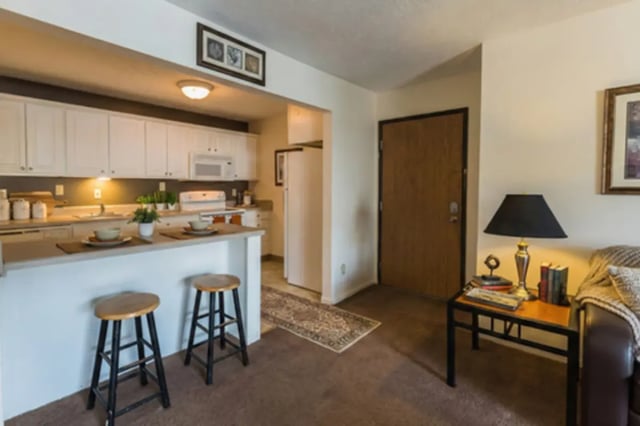 Kitchen island with stools and living room area Living Room at Waters Edge Apartments in East Lansing Student Accommodation