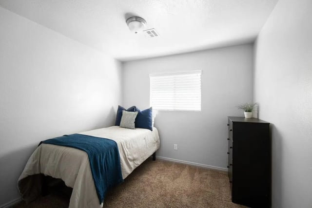 Bed with blue throw dresser with plant bedroom at 7th & University Apartments in St. George Student Accommodation
