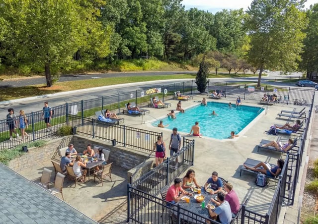 Poolside lounge chairs tables with people dining outdoor recreation area at Campus Hill Apartments
