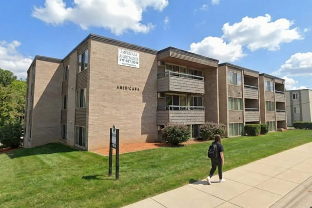 Brick apartment building with balconies student walking exterior at Americana Apartments in East Lansing Student Accommodation