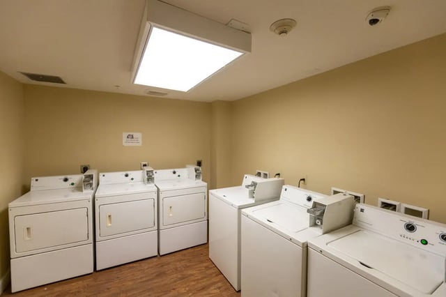 Multiple white washers and dryers with coin slots Laundry room at Central Place in Morgantown Student Accommodation