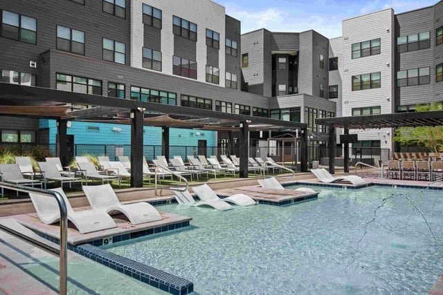 White lounge chairs in pool with modern building exterior. at Park Place Tempe in Tempe Student Accommodation