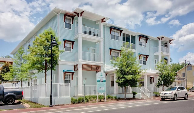 Light blue apartment building with balconies and cars exterior at Heritage Oaks Luxury Apartments in Gainesville Student Accommodation