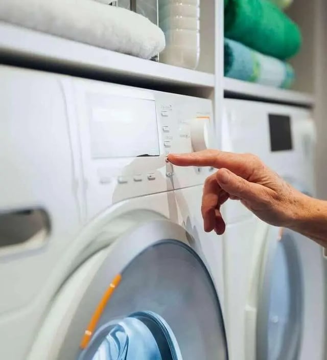 Hand pressing button on washing machine laundry area at The Den Apartments in Berkeley Student Accommodation