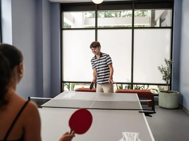 People playing ping pong near large windows playing area at Rambler Atlanta Apartments in Atlanta Student Accommodation