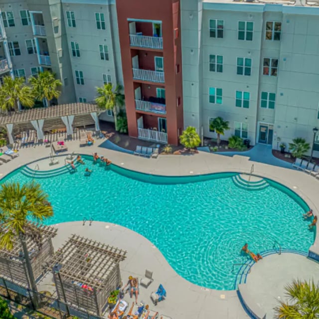 Pool with people lounging on chairs and swimming exterior at The Ascent in Conway Student Accommodation