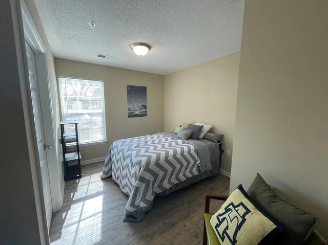Bed with gray chevron bedding chair pillows bedroom at Campus East Apartments in Greensboro Student Accommodation