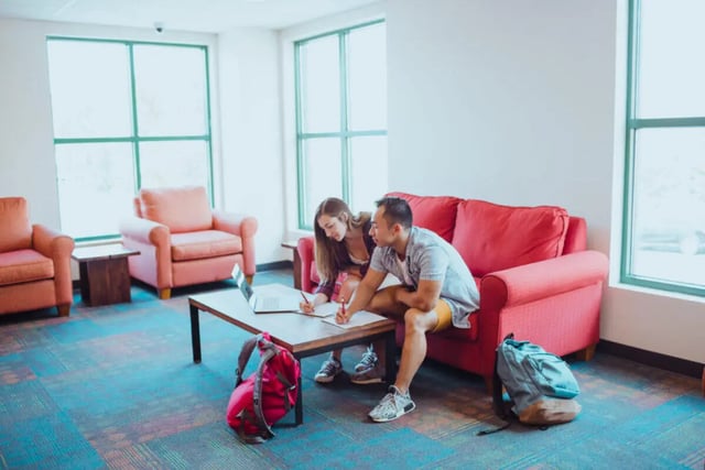 Students studying on sofa with backpacks living room at Copper Beech Commons Student Housing in Syracuse Student Accommodation