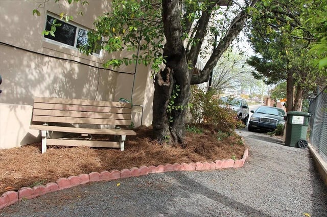 Wooden bench with trees cars and trash bin exterior at Barristers Hall in Macon Student Accommodation