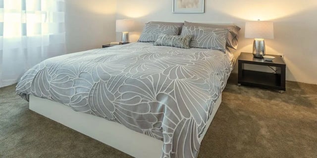 Bed with grey patterned duvet bedside tables and lamps bedroom at Baylor Arms in Waco Student Accommodation