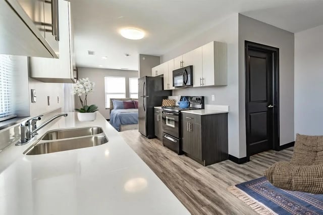 Kitchen sink refrigerator stove cabinets and bedroom living room at CitySide By Alexa in Bloomington Student Accommodation