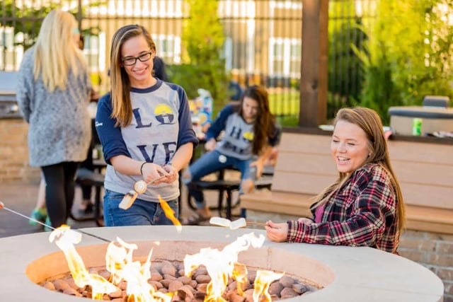 Students roasting marshmallows around fire pit outdoor area at Beacon Commons in Springfield Student Accommodation