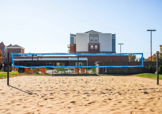 Beach volleyball court with seating and building exterior at Bear Village Apartments in Springfield Student Accommodation