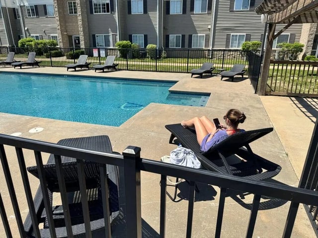 Poolside lounge chairs apartments and woman on lounge chair pool area at Crimson Villas in Pittsburg Student Accommodation