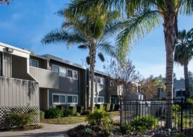 Apartment buildings with palm trees and fence exterior at Aggie Square Apartments in Davis Student Accommodation