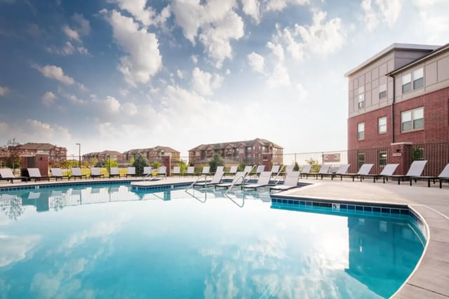 Pool with lounge chairs and apartment buildings exterior at Broadmoor Hills in Omaha Student Accommodation