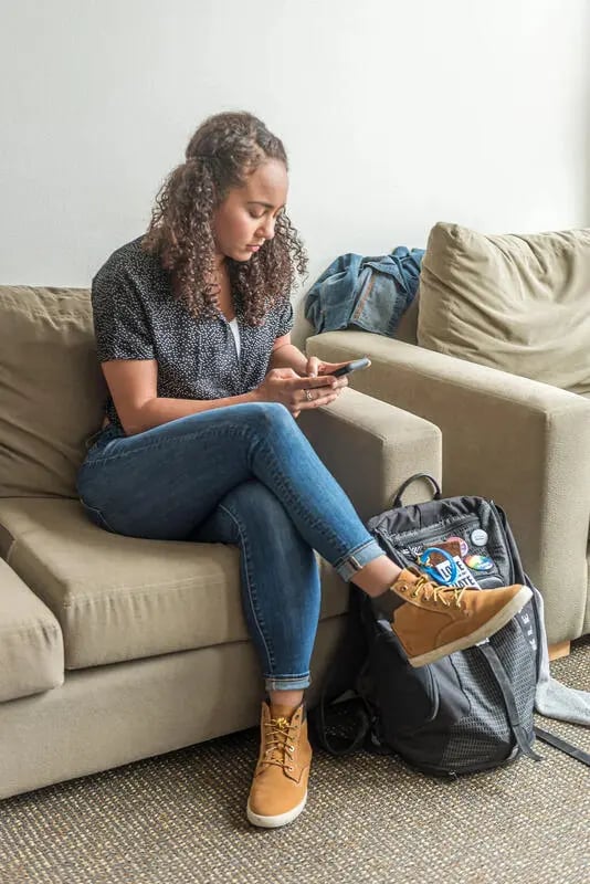 Girl on couch using phone near backpack Living room at The Douglas - Student Housing Apartments in Seattle Student Accommodation