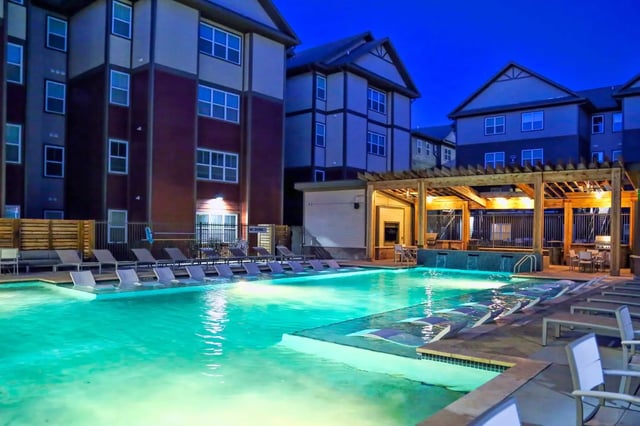 Apartment buildings by illuminated pool with lounge chairs exterior at The Bloc in Lubbock Student Accommodation