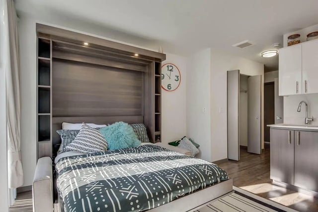 Bed with patterned bedding clock kitchen area bedroom at NORA Apartments in Seattle Student Accommodation