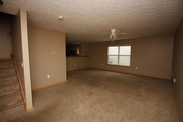 Carpeted living area with stairs and window Living room at Conner Crossing Apartments -"The Porches" in West Lafayette Student Accommodation