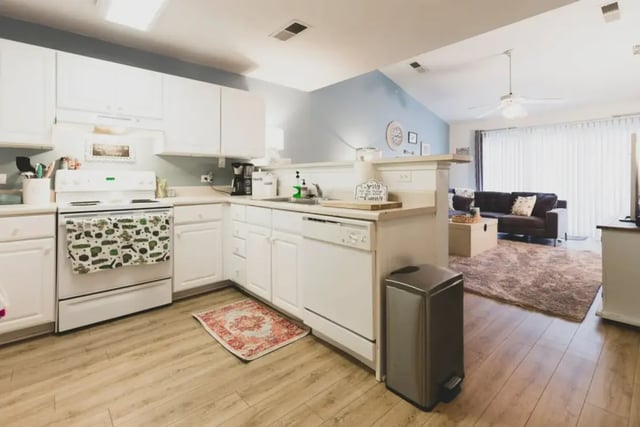 White kitchen with stove dishwasher and living area at Belmont Landing in Farmville Student Accommodation