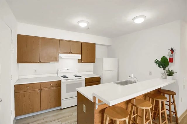Kitchen with white appliances brown cabinets counter bar stools kitchen at Cedar Lofts East Apartments in State College Student Accommodation