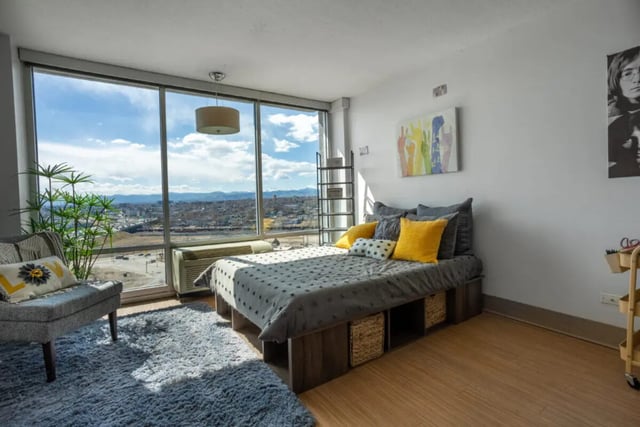 Bed with grey bedding yellow pillows grey chair bedroom at Assembly Student Living in Denver Student Accommodation
