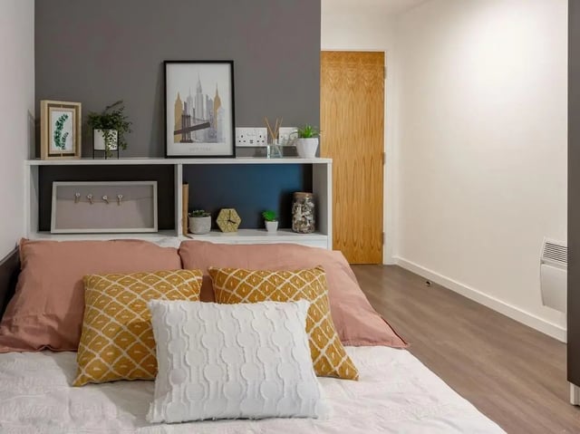 Bed with pink and patterned pillows bookshelf bedroom at Pavilion Court London in Wembley Student Accommodation